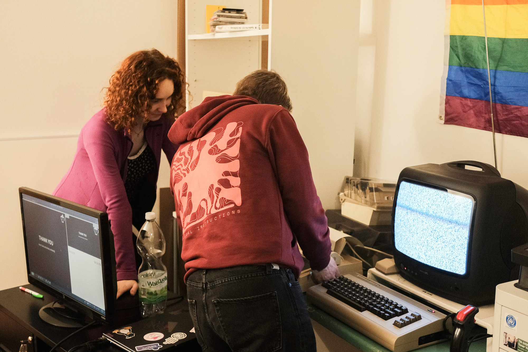 Two people (jupfi, noniq) are standing in front of an old CRT and C64 with a printer. They are working on the printer. 